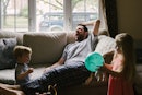 一个男人坐在沙发上打哈欠，他的两个孩子在他周围玩耍。万博体育app安卓版下载