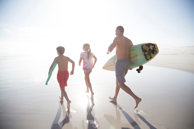 A dad and two kids on the beach with surfboards running toward the water.