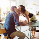 Wife leaning in to kiss husband across breakfast table 