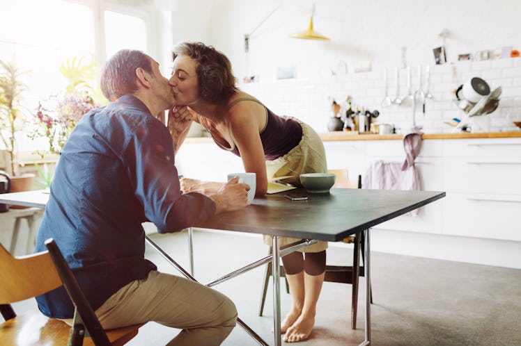 Wife leaning in to kiss husband across breakfast table 