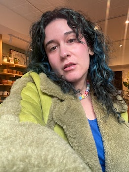 woman with glowing skin and blue hair wearing a green faux fur coat