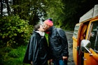 幸福的情侣在雨中亲吻，站在露营车旁