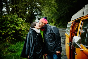 Happy couple kissing in the rain standing next camper van