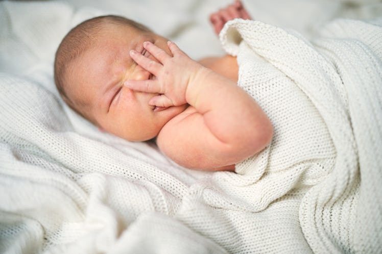 A hiccupping baby covering its mouth with its hand.