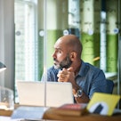 Bald man sitting at computer in office staring out the windo