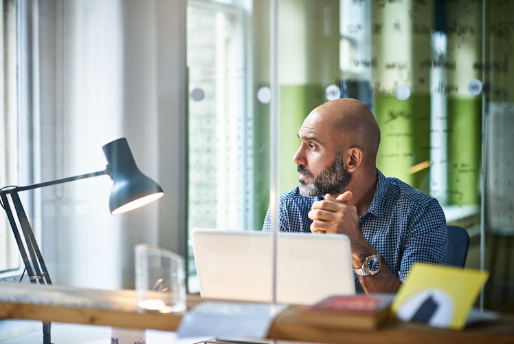 Bald man sitting at computer in office staring out the windo