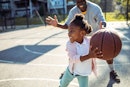 A girl playing basketball with her dad.