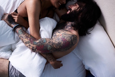 A man and woman in underwear, in bed, cuddling and smiling.