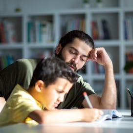 A child struggles to do his homework as his dad helps.