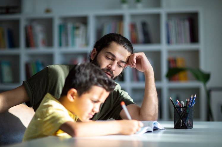 A child struggles to do his homework as his dad helps.