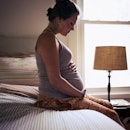 A pregnant person sitting on a bed, holding their belly.