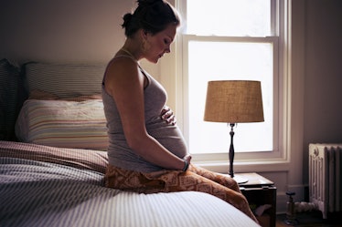 A pregnant person sitting on a bed, holding their belly.