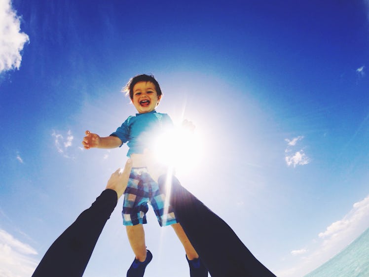 A dad's arms throwing a child into the air outside.