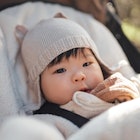 A baby in a hat and jacket in a stroller outside.