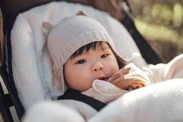 A baby in a hat and jacket in a stroller outside.