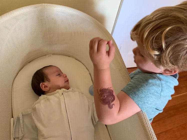 Baby rests in Snoo smart bassinet while older brother looks on.