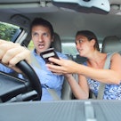 Woman showing phone to stressed out man driving car