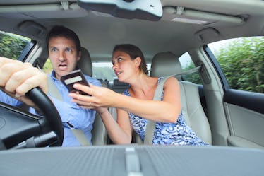 Woman showing phone to stressed out man driving car