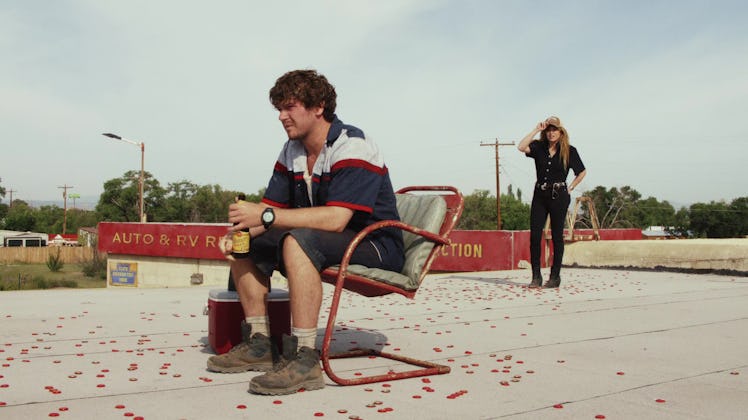 Colton Ryan sits on a roof while Natasha Lyonne stands behind him in Poker Face Episode 2