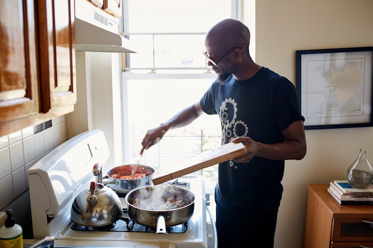 A man cooking at home, stirring a pot on the stovetop.
