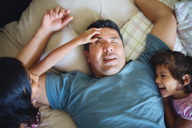 Two daughters wake up their father in his bed by lifting his eyelids.
