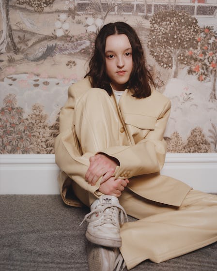 A portrait of Bella Ramsey sitting, wearing a buttercup yellow leather suit