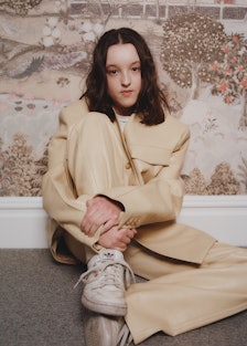 A portrait of Bella Ramsey sitting, wearing a buttercup yellow leather suit