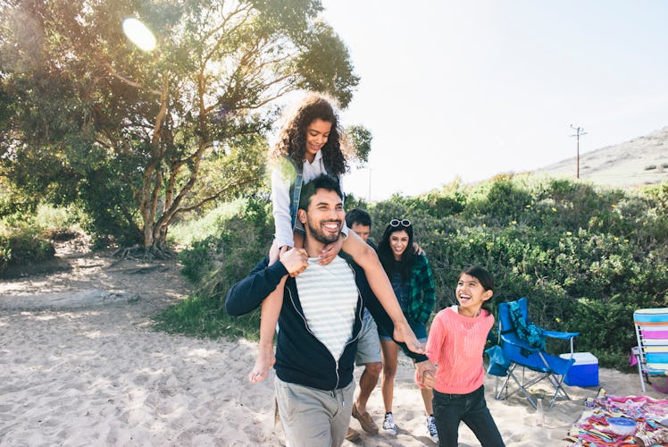 A dad with a child on his shoulders takes a walk with his family through a sandy nature area.