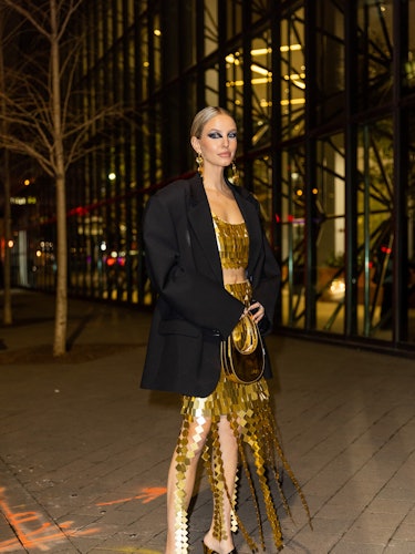 Leonie Hanne wears golden dress, earrings, Coperni bag, black oversized blazer outside Simkhai durin...