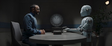 Dr. Pershing (Omid Abtahi) sits across a table from a New Republic droid in The Mandalorian Season 3...