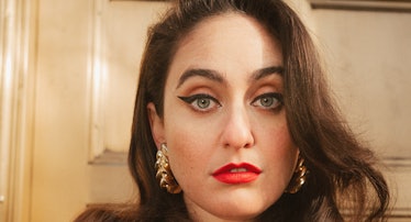 Comedian Catherine Cohen wearing a blazer, red lipstick and gold earrings.