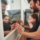 A dad and baby looking at themselves in a mirror and smiling.