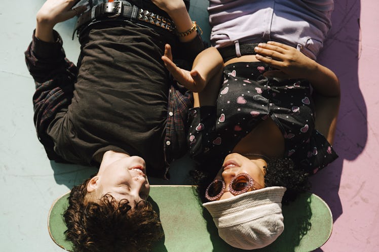 Two teens lying on the ground with their heads on a skateboard.