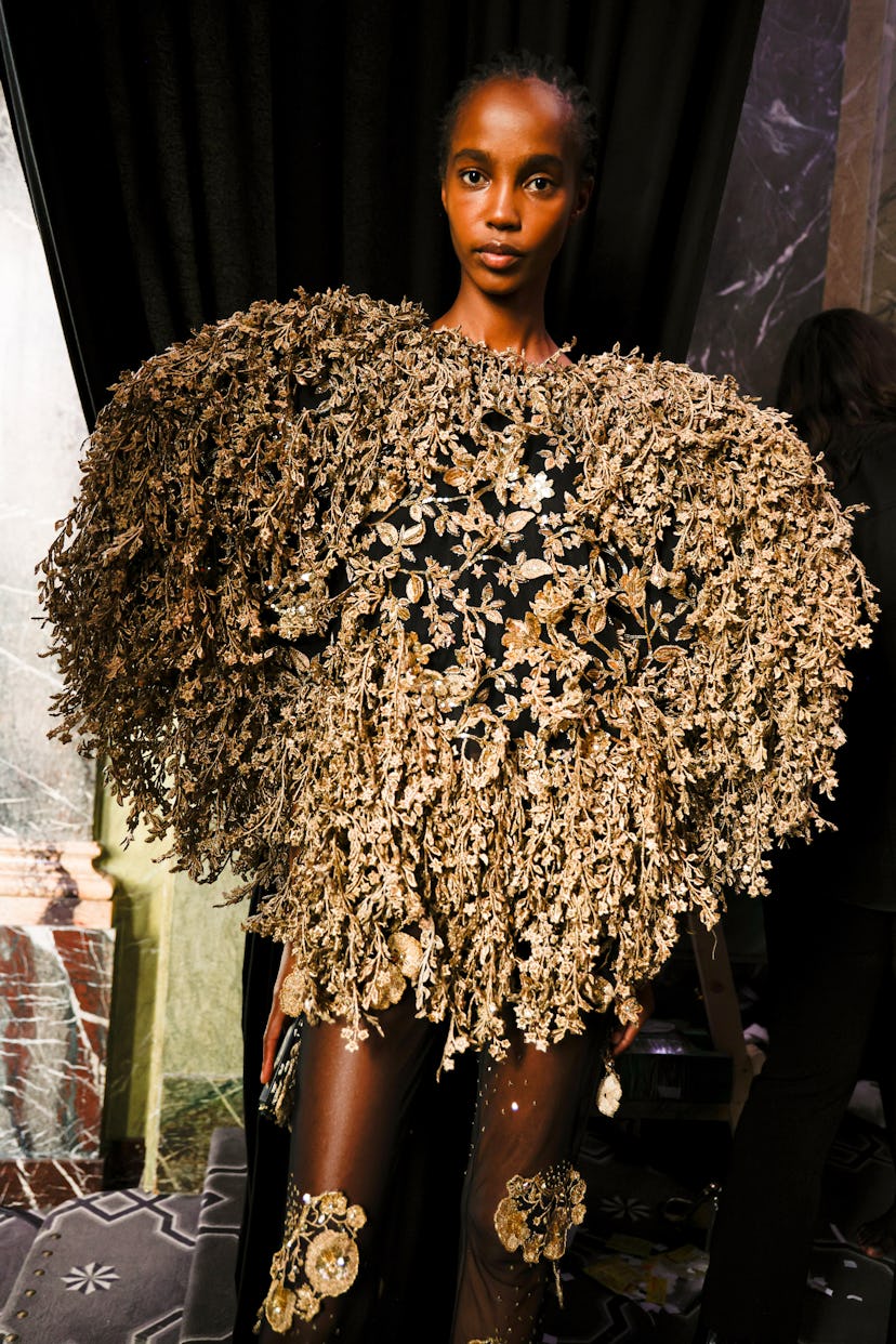 a model wearing a cape constructed of thousands of gold embroidered leaves
