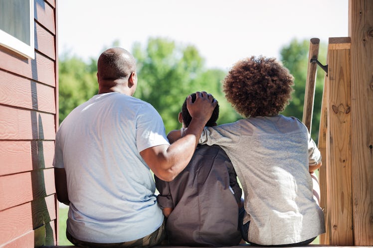 A child sitting between two parents on a porch step, facing away.