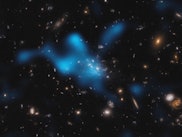 a blue cloud of gas against a field of stars and galaxies in shades of white to orange, on a black b...