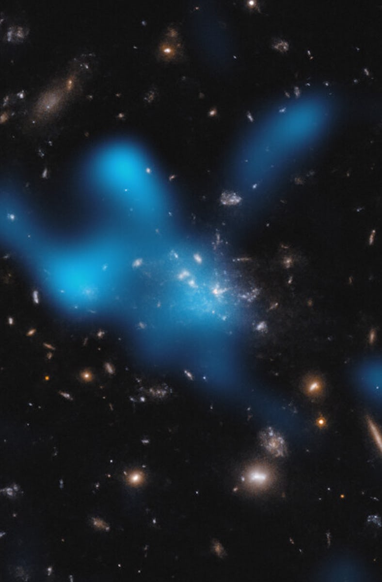 a blue cloud of gas against a field of stars and galaxies in shades of white to orange, on a black b...
