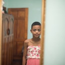 A trans kid in a dress looking in a mirror.