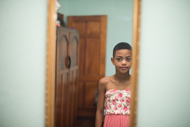 A trans kid in a dress looking in a mirror.