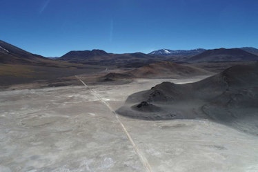 photo of a flat, white ground with dark mountains in the background and a blue sky above