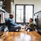 A dad and child sitting on the kitchen floor, talking.
