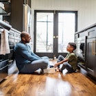 A dad and child sitting on the kitchen floor, talking.