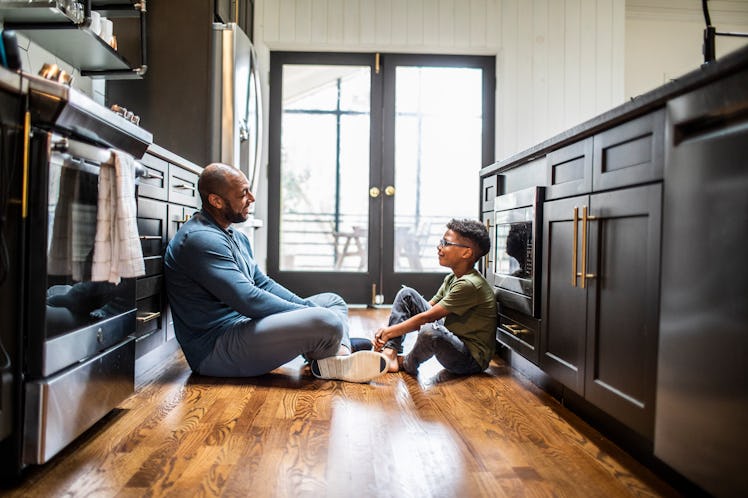 A dad and child sitting on the kitchen floor, talking.