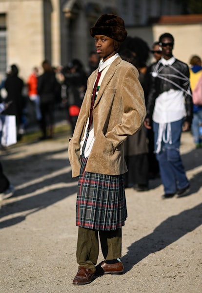 A guest is seen wearing a tan jacket, white shirt, red tie, plaid skirt and brown hat outside the Gi...