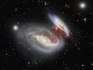 two spiral galaxies in the center of a black background, with streamers of red gas stretching betwee...