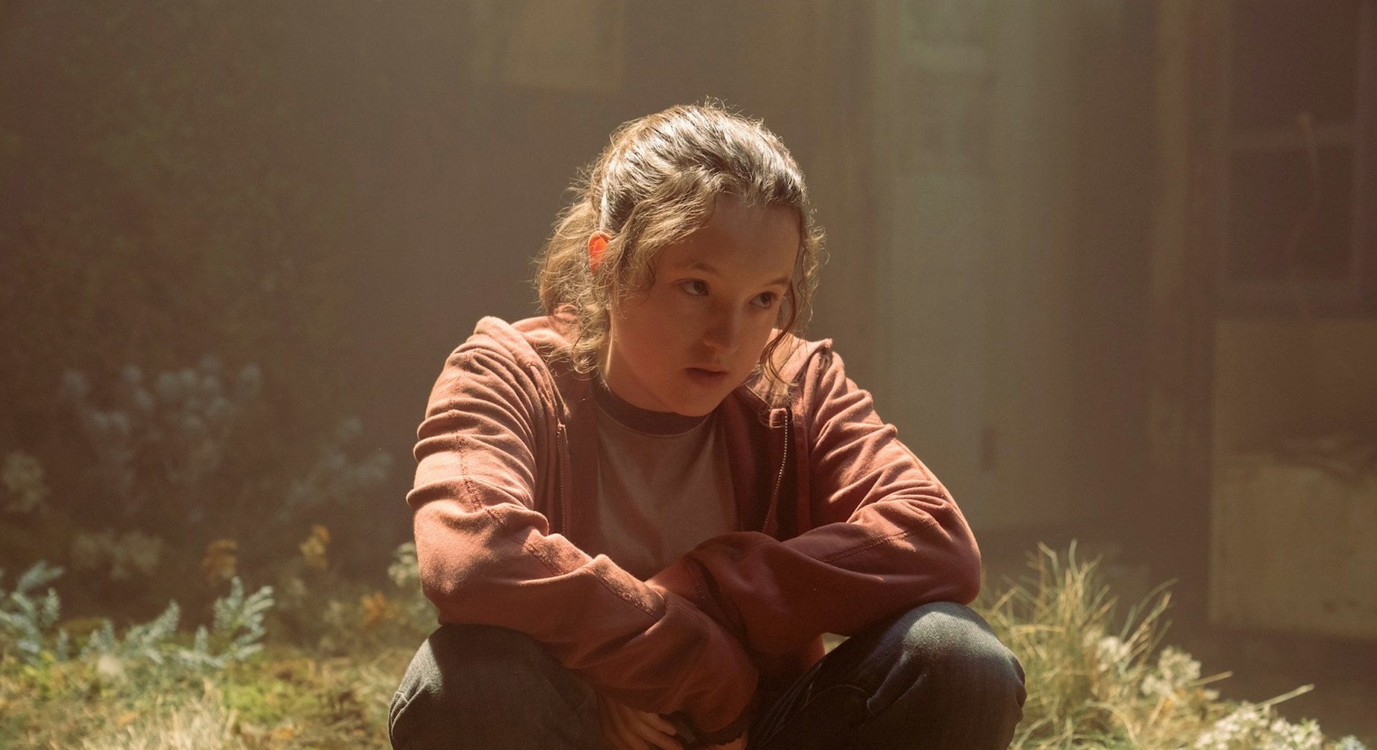 Bella Ramsey as Ellie in The Last of Us, sitting in a sad building 