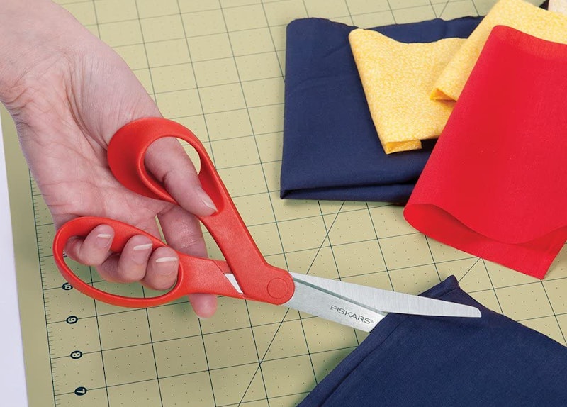 A left-handed person uses left handed scissors to cut fabric.