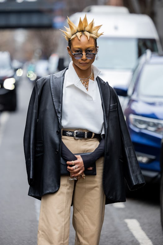 Actress Tati Gabrielle with blonde gelled hair style wears leather jacket, beige pants, white shirt ...