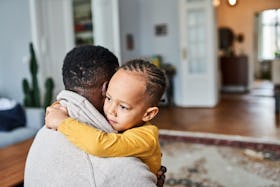 A Black child hugging their father at home.