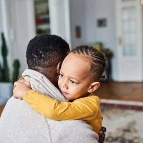 A Black child hugging their father at home.